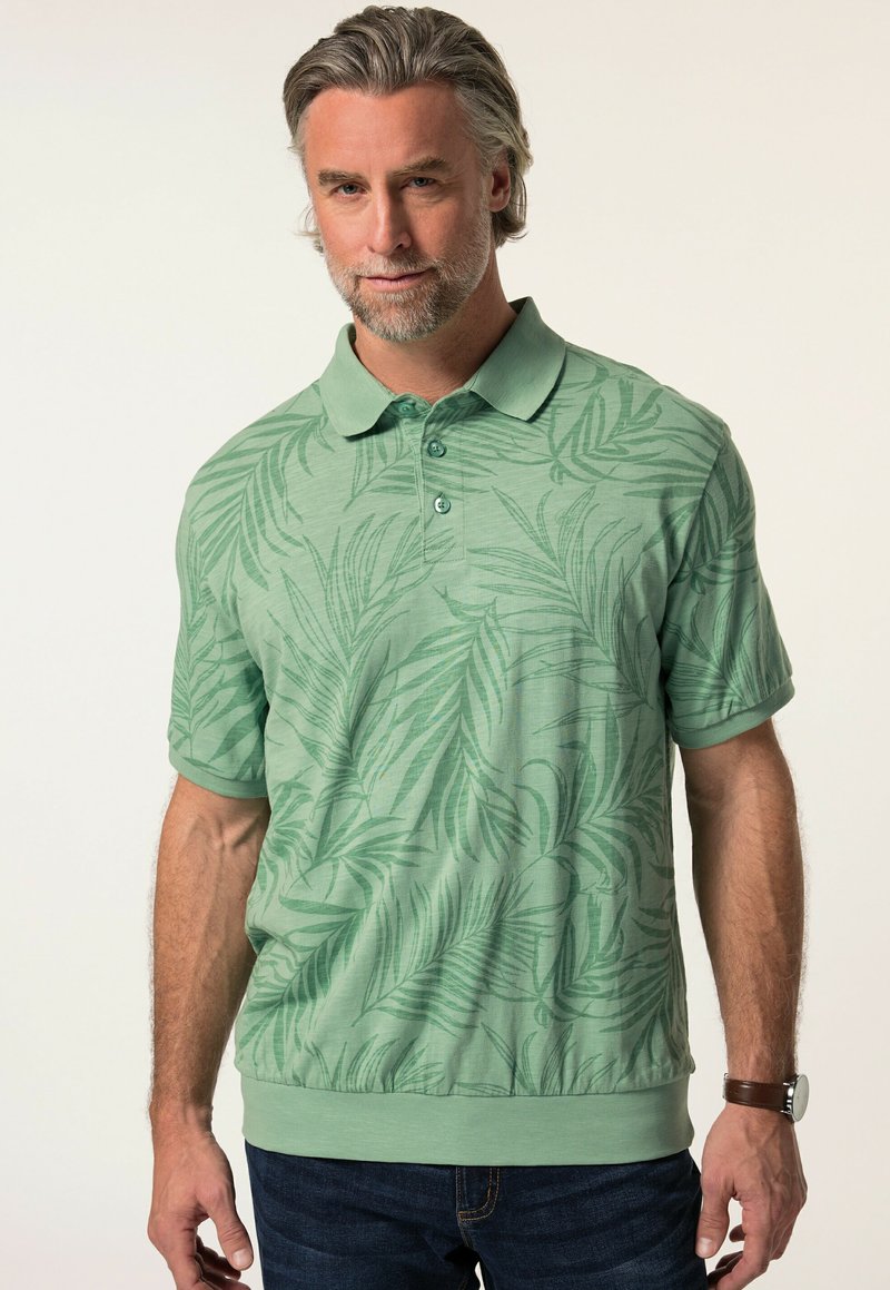 Zelená polo tričko s jemným vzorem palmových listů. Krátké rukávy, zapínání na knoflíky a uvolněný střih. Nosené s tmavými džíny.