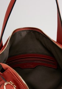 Otwarta czerwona skórzana torebka z złotym zamkiem błyskawicznym, czarnym materiałowym wnętrzem oraz wewnętrzną kieszenią na zamek z metką marki L.CREDI.