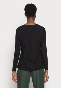 Haut noir à manches longues avec un col rond, présentant une texture drapée et une coupe décontractée, associé à un pantalon vert à jambes larges.