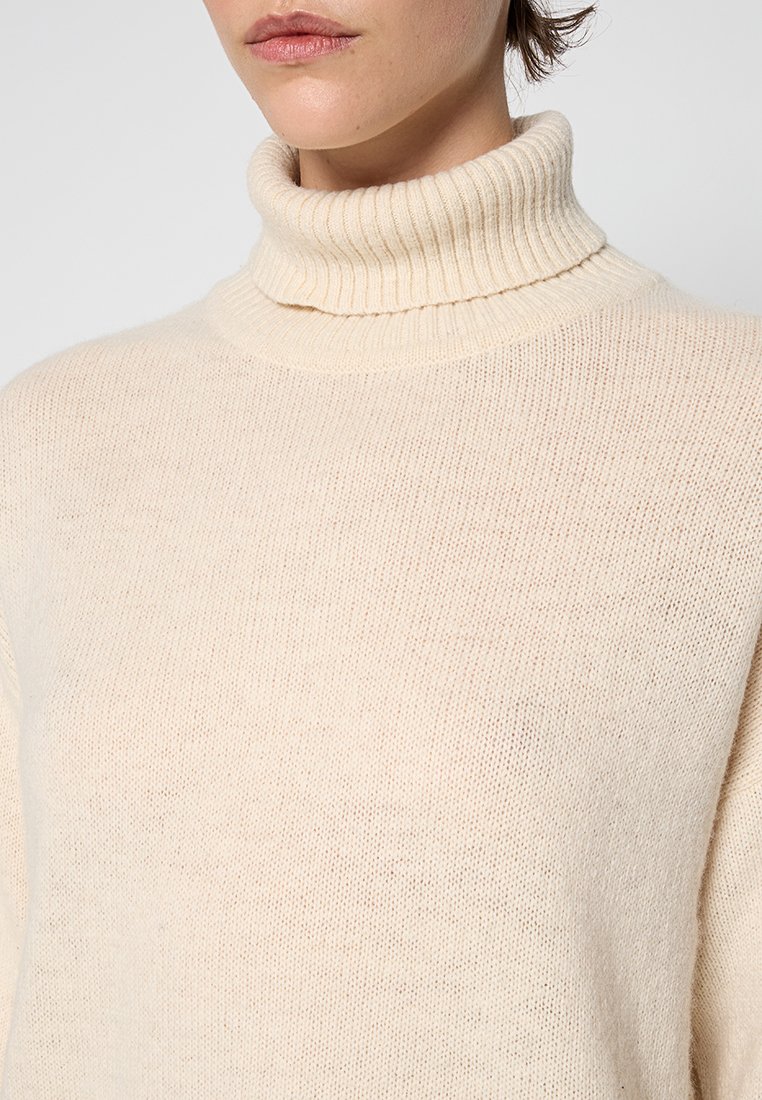 Cremfarbener Rollkragenpullover aus strukturiertem Strickstoff. Verfügt über einen hohen gerippten Kragen und eine lockere Passform, die ein weiches, leichtes Erscheinungsbild zur Schau stellt.