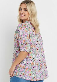 Blommig skjorta med mångfärgade blommor i nyanser av rosa, orange och grönt. Har puffärmar och en lös passform, tillverkad av lättviktsmaterial.