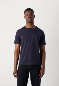Marineblaue T-Shirt mit kurzen Ärmeln aus weicher Baumwolle, mit einem einfachen Rundhalsausschnitt und einem lässigen Schnitt, kombiniert mit dunklen Jeans.