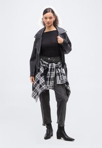 Γυναίκα που φοράει μαύρο δερμάτινο μπουφάν, μαύρο τοπ, σκουρόχρωμο τζιν, μαύρα μποτάκια στον αστράγαλο και ένα ασπρόμαυρο καρό πουκάμισο δεμένο γύρω από τη μέση της.