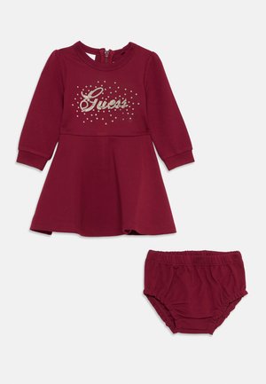 Maroon pitkähihainen mekko, jossa on kimalteleva "Guess"-logo ja flare-mallinen hame, yhdistettynä joustavan vyötärön lastenhaalareihin. Pehmeää puuvillamateriaalia.
