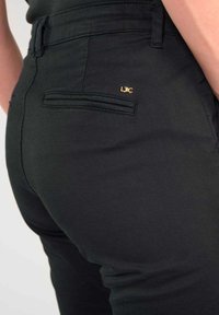 Zwarte broek met een slank ontwerp, een achterzak met een subtiele logodetail en een gladde textuur. De tailleband is ook zichtbaar.