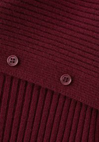 Tessuto bordeaux lavorato a maglia con una texture a coste e due bottoni tondi e scuri. Il tessuto presenta strisce verticali per aggiungere profondità.