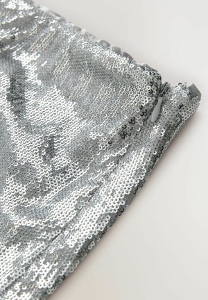 Close-up of silver sequin fabric with a closed zipper pull against a plain light background.
