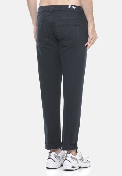 Pantaloni di cotone blu scuro con taglio dritto, risvolti e tasche posteriori; abbinati a scarpe sportive bianche e argentate.