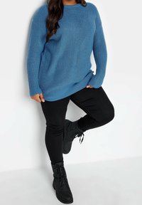 Blå stickad tröja med ribbat mönster, långa ärmar och rundad halsringning, kombinerad med svarta skinny jeans och svarta snörskor.