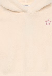 Crèmekleurige hoodie gemaakt van zacht, fluffy materiaal, met een geborduurde roze steraccent op de voorkant. Capuchonontwerp met een gestructureerde afwerking.