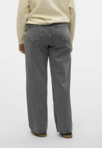 Jeans largi din denim gri, cu o vopsire medie, având buzunare la spate și un croi relaxat, asortați cu un sweatshirt bej și pantofi maro.