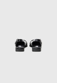Black patent leather sandals with an open back, featuring a buckle detail, flat soles, and a smooth texture.