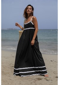 Czarna długa sukienka maxi z białą koronkową lamówką przy krawędzi i gorsecie. Posiada cienkie ramiączka i luźny, zwiewny fason. Noszona na plaży.
