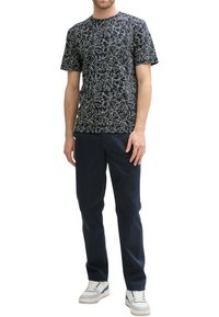 T-shirt à manches courtes marine avec un motif floral blanc, associé à un pantalon sombre et des baskets blanches. Tissu lisse, design col rond.