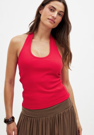 Red ribbed halter top with a scoop neckline and fitted design. Paired with a brown pleated skirt, showcasing a smooth texture and flowing fabric.
