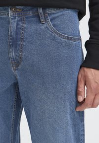 Traperice svijetloplave boje, s klasičnim dizajnom pet džepova, kontrastnim šavovima i uskim krojem oko struka i bedara.