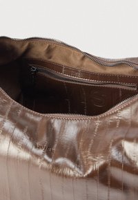 Geantă maro din piele cu finisaj lucios, cu o suprafață texturată și un buzunar interior cu fermoar. Căptușită cu un material maro neted.