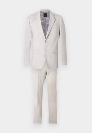 Jasnobeżowy dwuczęściowy garnitur męski z klapą z wcięciem, marynarką na dwa guziki, kieszeniami z patkami oraz dopasowanymi spodniami na jednolitym tle.