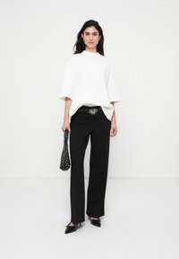 Λευκό φαρδύ μπλουζάκι, μαύροι ψηλόμεσοι παντελόνες, ασημένια αγκράφα ζώνης σε σχήμα καρδιάς, μαύρα μυτερά παπούτσια και μαύρη και λευκή τσάντα με πουά.