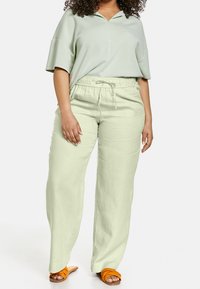 Haut ample vert clair avec col en V et manches courtes, associé à un pantalon vert clair avec cordon de serrage ; sandales à enfiler orange.
