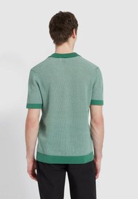 Zielona krótko rękawowa koszulka polo z dzianiny z teksturowanym wzorem, z jednolitą zieloną kołnierzykiem i mankietami, z prostym hemem i luźnym krojem.