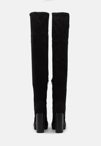 Černé semišové kozačky nad kolena s přiléhavým střihem, vysokými robustními podpatky a bočními zipy pro zapínání.