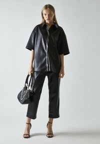 Top de cuero sintético negro con botones en la parte frontal, mangas cortas y pantalones negros a juego. Incluye un pequeño bolso con detalle de cadena.