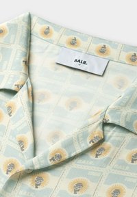 Korte mouwen shirt in lichtgroen, met een herhaald patroon van stempels met schedels en zonmotieven, op zachte stof met een kraag.