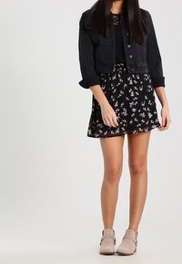 Veste en denim noir courte portée sur un haut noir, accompagnée d'une jupe imprimée fleuri noire et rose. Des bottines beiges claires à la cheville complètent le look.