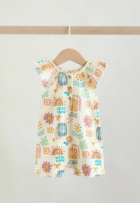 Combinaison bébé avec manches courtes volantées, boutons sur le devant et motifs abstraits colorés comprenant des arcs-en-ciel et des fleurs, suspendue sur un cintre en bois.