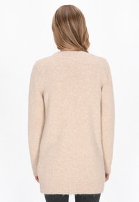 Maglione beige a maglia con una texture morbida, maniche lunghe e scollatura rotonda, caratterizzato da un orlo posteriore leggermente più lungo e polsini a coste.