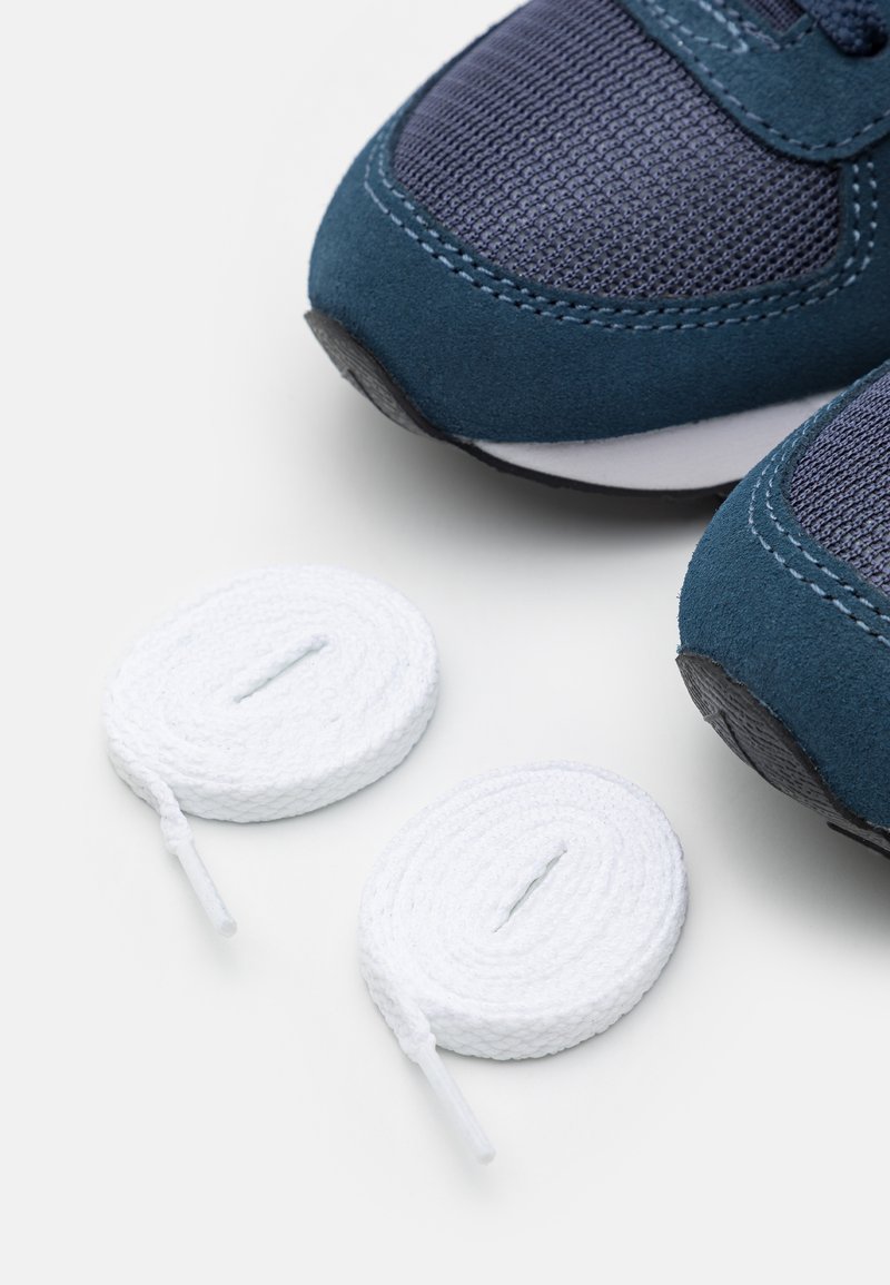 Zapatillas deportivas de color azul oscuro con texturas de malla y ante, que presentan cordones redondos blancos y suelas de goma negras, dispuestas sobre un fondo claro.