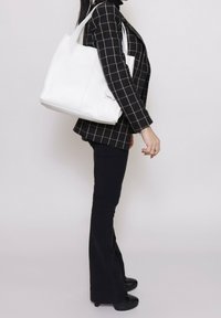 Borsa a mano in pelle bianca con manici resistenti, forma rettangolare e texture liscia. Abbinata a un blazer a quadri neri e pantaloni a zampa.