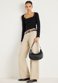 Moteris dėvi juodą ilgomis rankovėmis palaidinę, smėlio spalvos plačias kelnes, juodą kniedėtą diržą, juodus aštriais galiukais batelius, laiko juodą pusmėnulio formos rankinę.