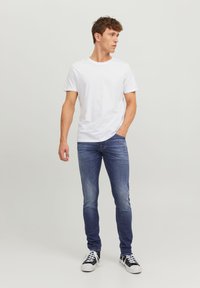 T-shirt en coton blanc assortie à un jean en denim bleu, avec une coupe slim et des détails délavés, complétée par des baskets basses noir et blanc.