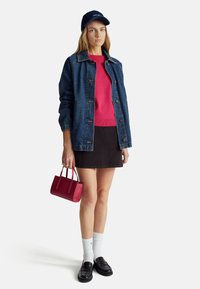 Giacca di jeans, maglione rosa, gonna nera, calzini bianchi e mocassini neri. Tiene una piccola borsa rossa. Design semplice e vestibilità casual.