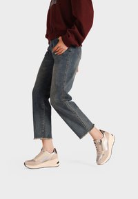 Sneakers platform beige con accenti metallici, chiusura con lacci e materiali testurizzati, abbinati a jeans in denim blu corti.