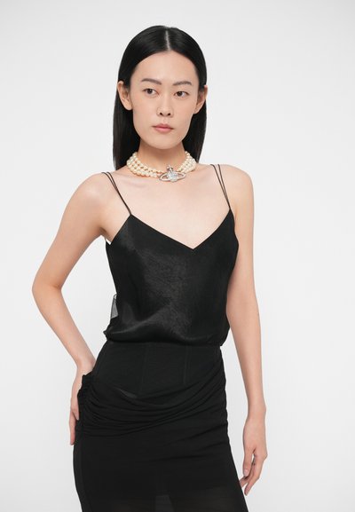 Camisola de cetim preta com alças finas, decote em V, combinada com uma saia preta franzida. Realçada por um colar de pérolas em camadas com um detalhe de cristal.