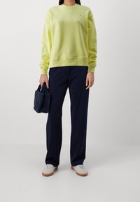 Neon gele katoenen sweatshirt met een geribbelde ronde hals, gecombineerd met navy wijde broek en een kleine navy gestructureerde handtas.