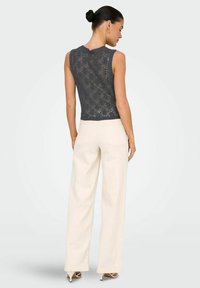 Haut sans manches en tricot dentelle gris foncé, associé à un pantalon large beige taille haute et des escarpins beiges pointus. Design minimaliste.