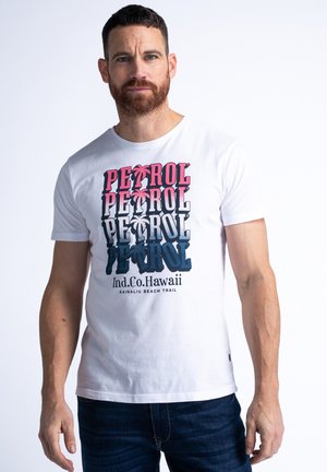 Fehér, rövid ujjú póló réteges grafikai dizájnnal, amelyen a "PETROL" felirat rózsaszín és kék árnyalatokban, valamint pálmafák kiemelésével látható.