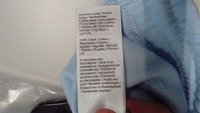 Világoskék szövetcímke, amelyen ápolási utasítások és anyagok részletei találhatók, több nyelven, beleértve a "100% Pamut" feliratot.
