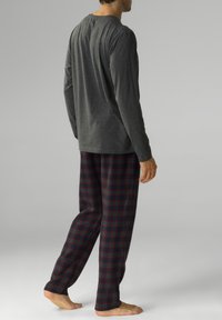 Ciemnoszara bluzka z długim rękawem w połączeniu z piżamowymi spodniami w kratkę w ciemnym granacie, zieleni i czerwieni. Miękka tkanina, luźny krój i lekka konstrukcja.