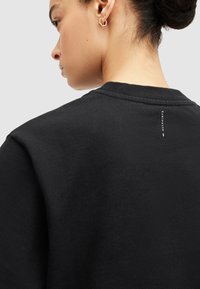 Melna sporta krekla ar ribotu apkakli, mīkstu tekstūru un nelielu drukātu logo detaļu aizmugurē. Elegants, ikdienišķs dizains.