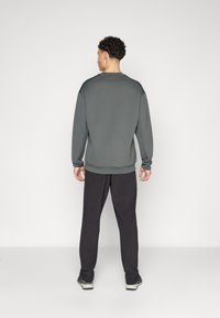 Herren Grauer Sweatshirt mit Struktur, gerippten Bündchen und Saum, kombiniert mit dunklen Hosen und Sportschuhen, von hinten betrachtet.