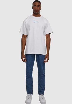 Hvit bomull t-skjorte med rund hals og korte ermer, med en blå brodert logo. Kombinert med blå denimjeans og hvite sneakers.