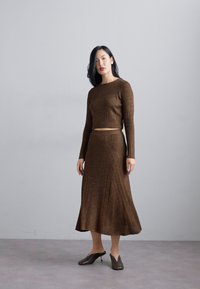 Brown ribbed knit two-piece set featuring a cropped long-sleeve top and a flared midi skirt. Worn with pointed brown shoes.