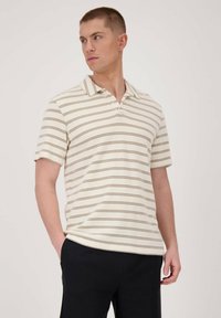 Camisa polo crema con rayas horizontales marrones, textura acanalada, mangas cortas y cuello clásico, combinada con pantalones oscuros.