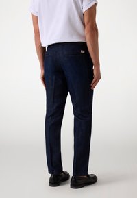 Temno modri kavbojki s slim fit krojem, z zadnjimi žepi in gladko teksturo. Par črnih čevljev dopolnjuje obleko.