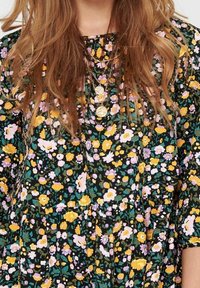 Vestido negro con estampado floral que presenta flores amarillas, rosas y blancas. Tela fluida con escote redondo y cintura fruncida. Material ligero y texturizado.